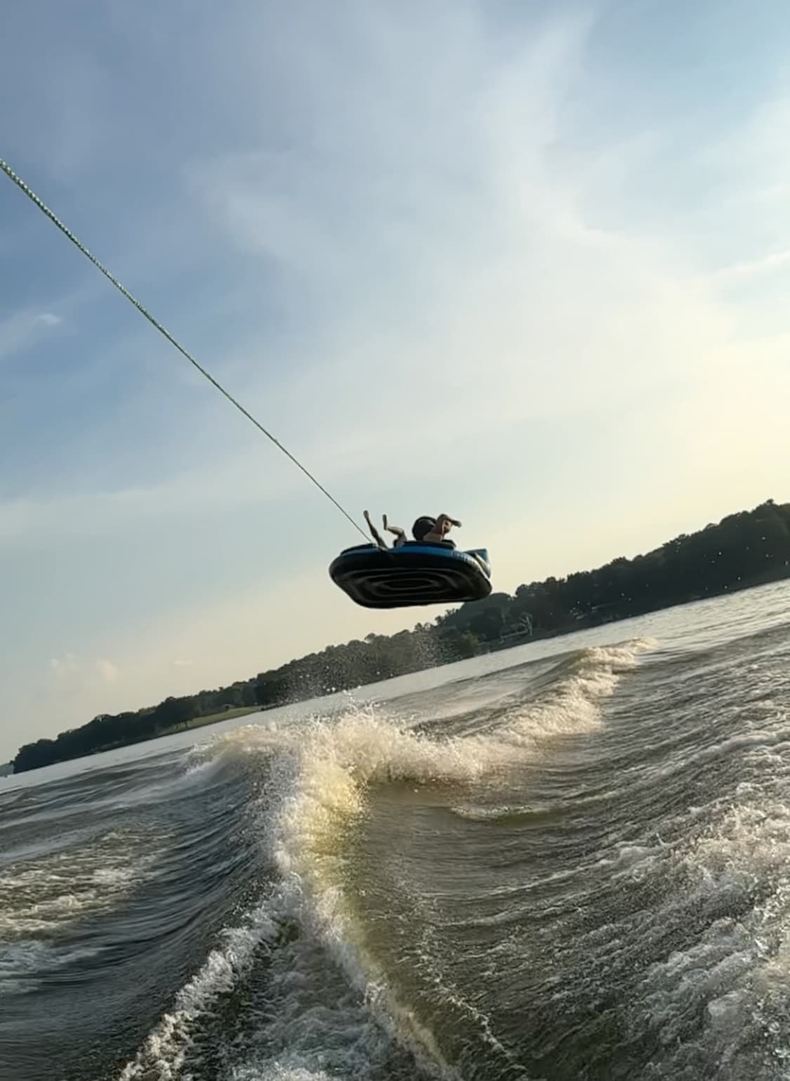 Person on an inflatable tube catching air high above a boat's wake on a sunny lake.